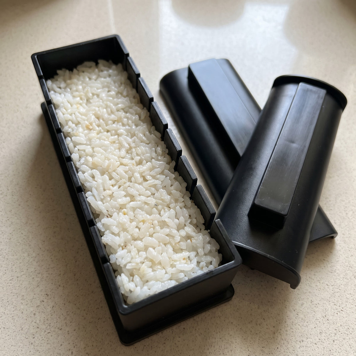 10-Piece Sushi Mold Kit for Rolls Nigiri and Maki - close-up of the black plastic roll mold packed with sushi rice beside its press lids