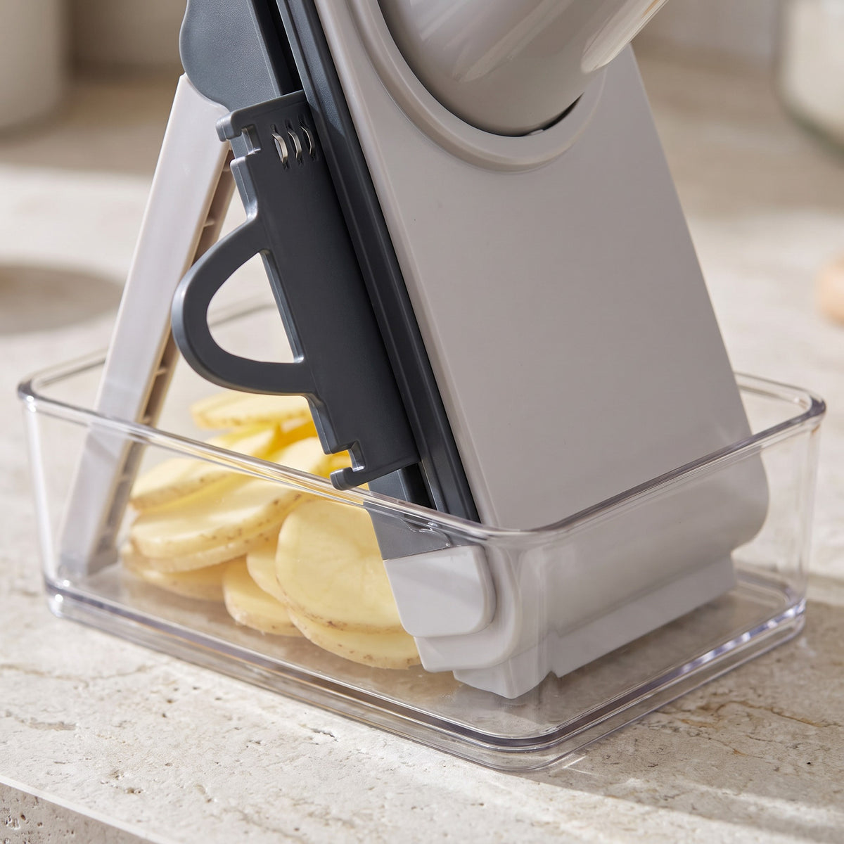 4-in-1 Vegetable Slicer for Potatoes and Onions - close-up of the blade plate and the clear container catching potato slices