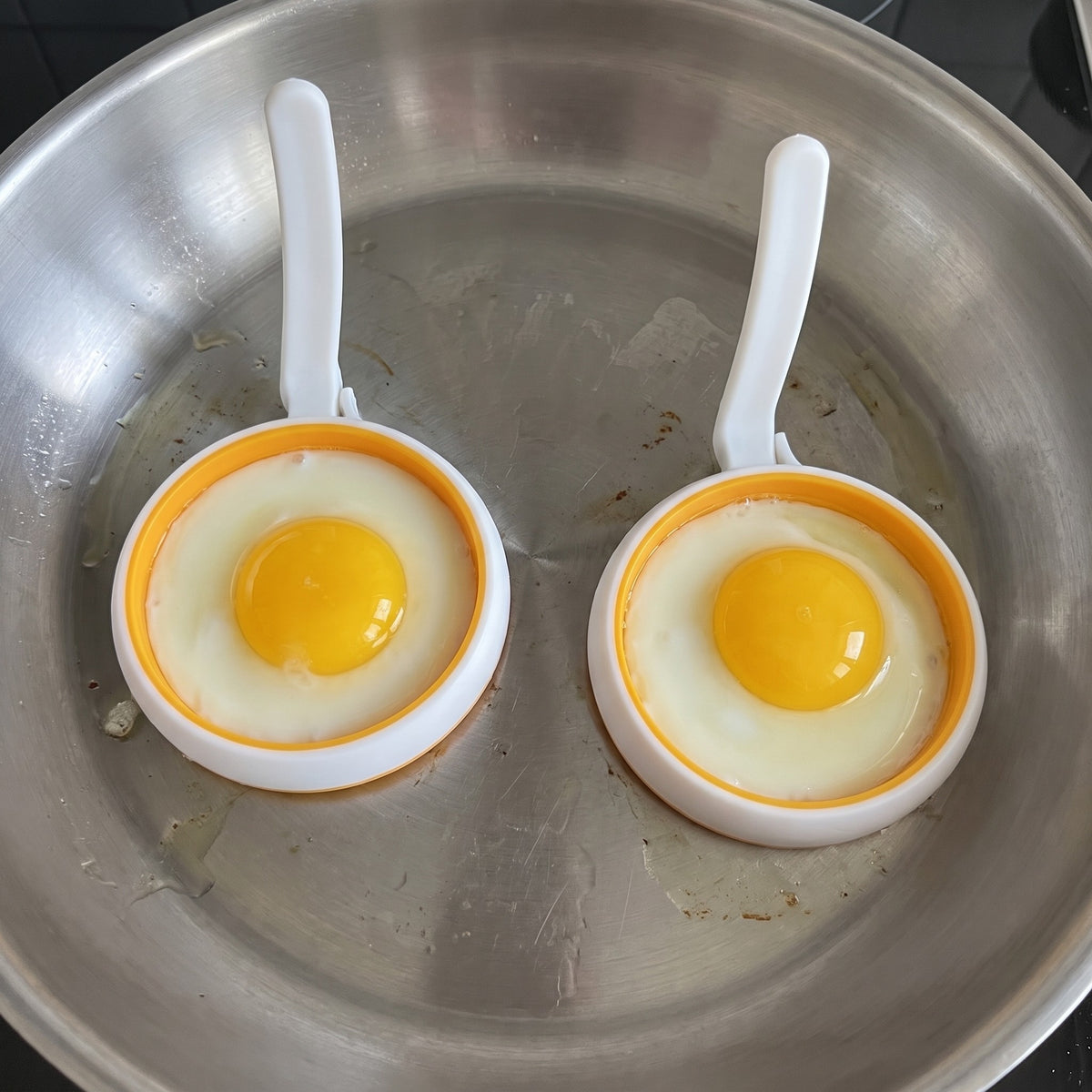 4-Inch Silicone Egg and Pancake Rings for Breakfast Sandwiches in use, frying two round eggs in a pan