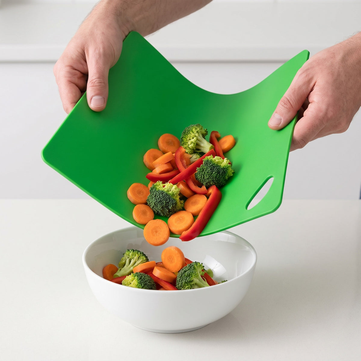 6-Piece Flexible Color-Coded Cutting Mat Set with Hanging Handles in use, bending the green mat to pour vegetables into a bowl