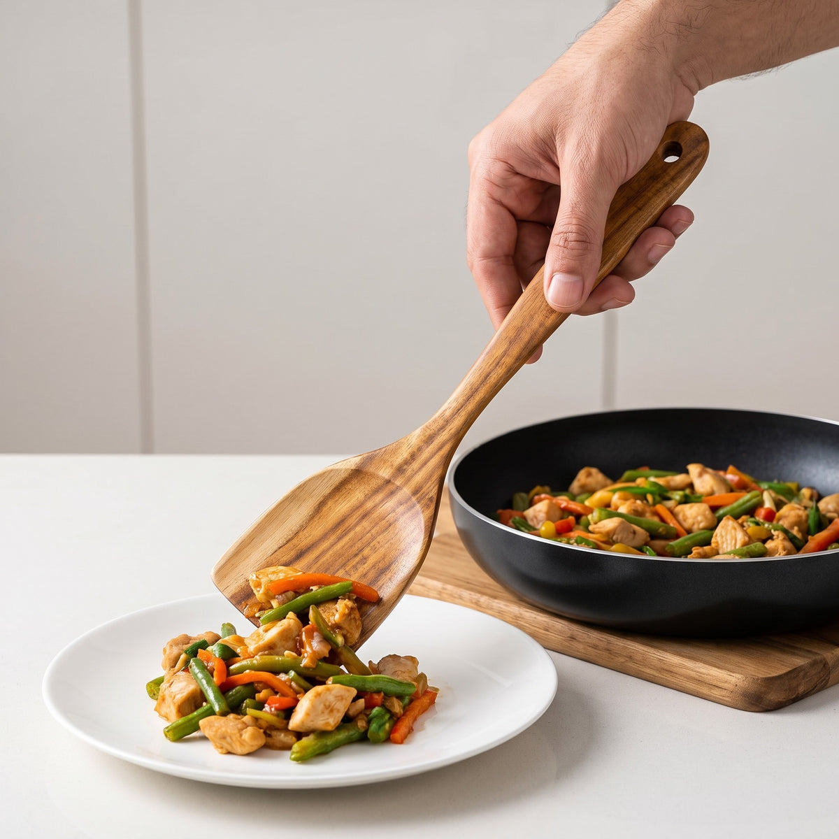 7-Piece Teak Wood Cooking Utensil Set for Nonstick Cookware in use, serving a stir-fry from a non-stick pan with the teak turner