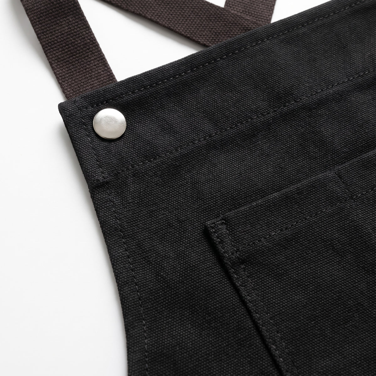 Cross-Back Kitchen Apron with Front Pockets and Waist Tie - close-up of the black canvas, snap button and brown strap