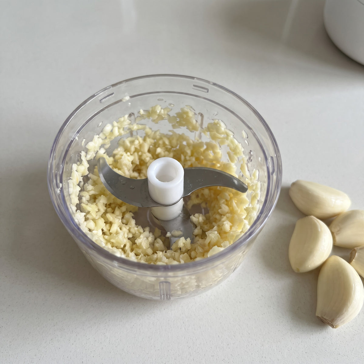 Mini Electric Garlic Chopper with Clear 250 ml Bowl - close-up of the stainless steel blades and minced garlic in the clear bowl