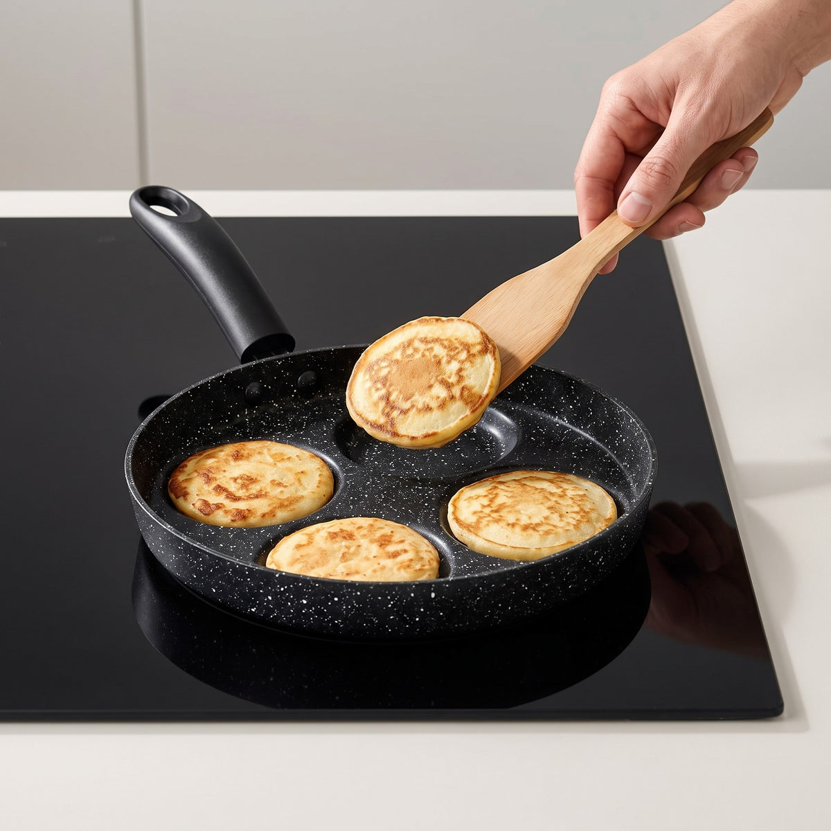 Multi-Cup Non-Stick Pancake Pan for Eggs and Blinis in use, lifting a golden pancake from one of the four cups