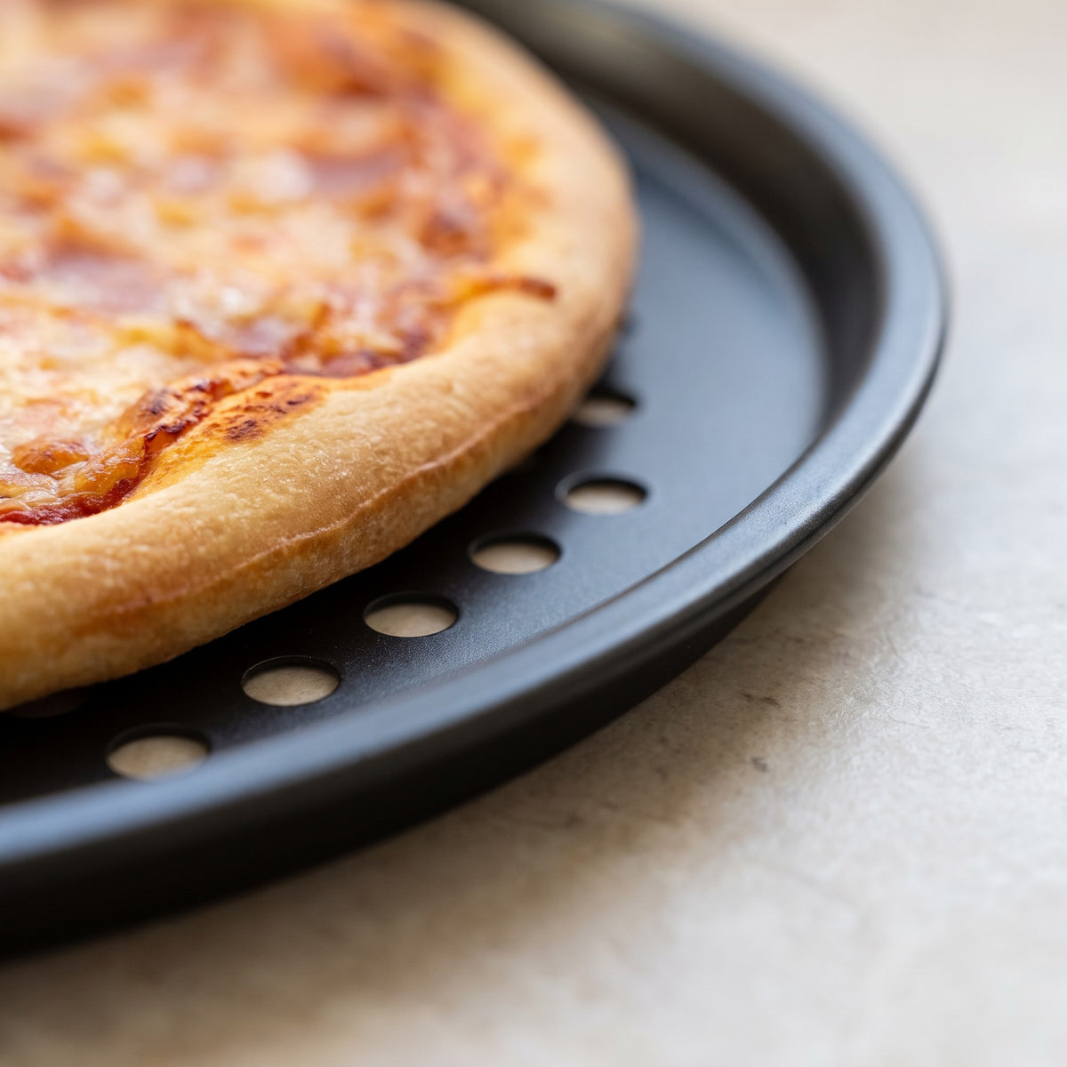 Perforated Non-Stick Carbon Steel Pizza Pan for Crisp Crusts - close-up of the perforated non-stick carbon steel rim under a baked crust