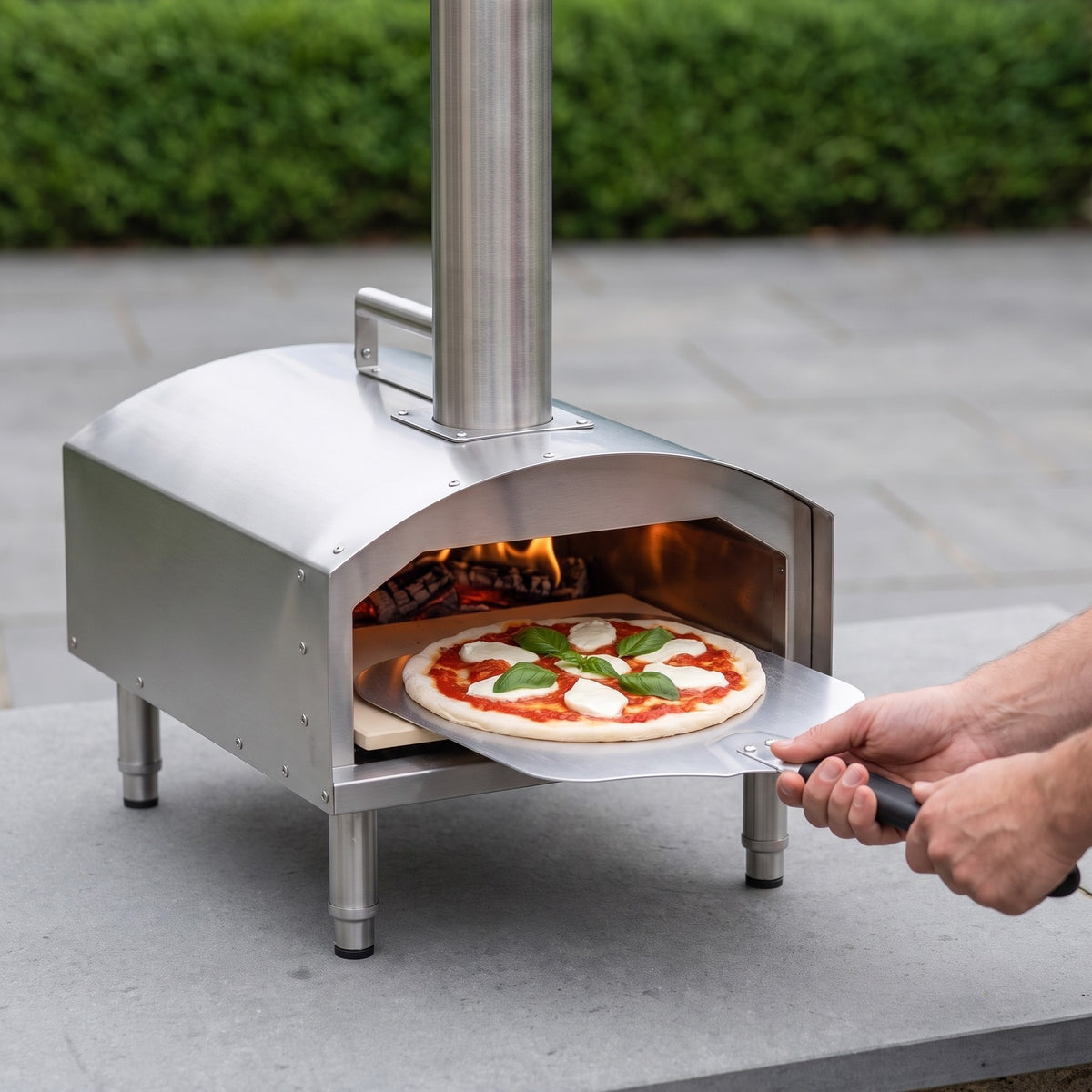 Portable Wood Pellet and Charcoal Pizza Oven with Stone and Peel in use, sliding a margherita pizza into the oven on a patio