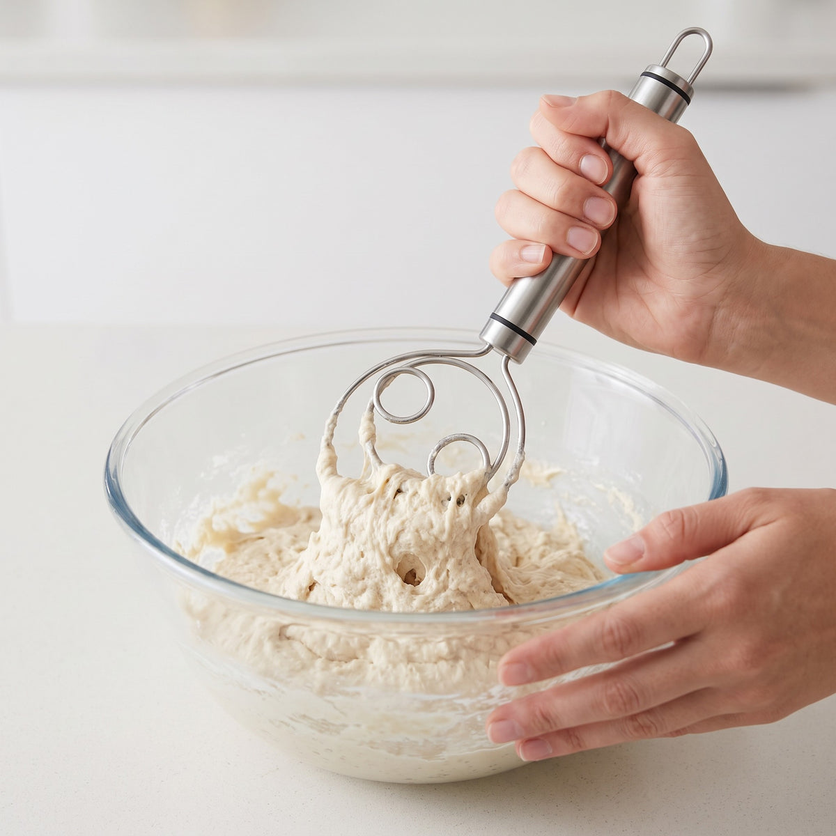 Stainless Steel Dough Whisk with Ergonomic Handle in use, mixing bread dough in a glass bowl